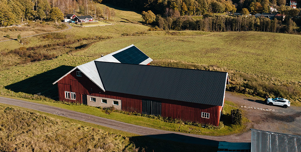 Röd lantgårdsbyggnad med solpaneler installerade av ZolarTech på taket, belägen i ett grönt landskap med skog i bakgrunden.